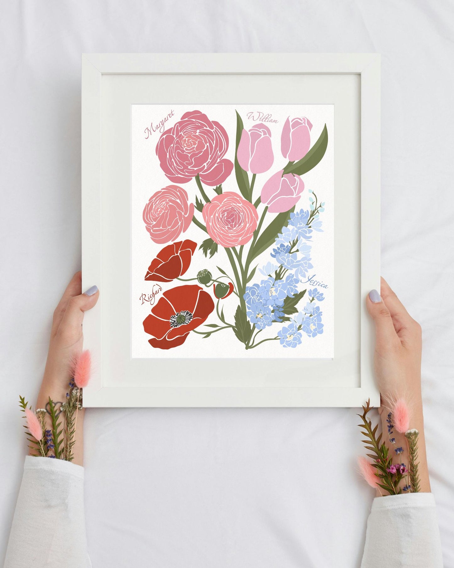 Framed floral artwork with pink, red, and blue flowers held by hands on a white background